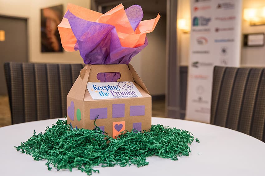 Decorated cardboard house box with colorful tissue paper on a table surrounded by green filler